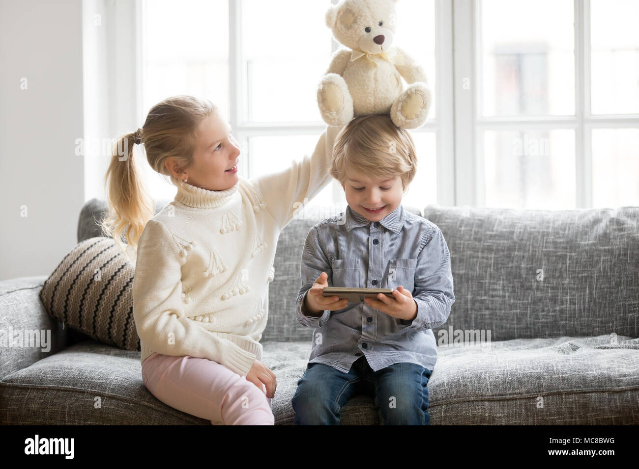 Happy Little Brother Holding digital Tablet während Schwester spielen mit Spielzeug Teddybären zu Hause, lächelnd Kinder Jungen und Mädchen gemeinsam Spaß in sittin Stockfoto