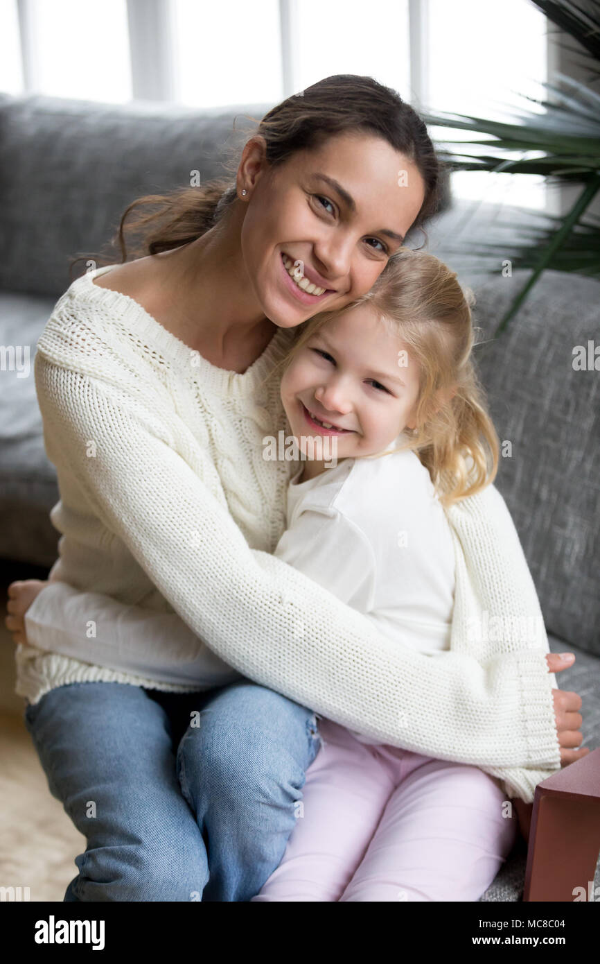 Gerne alleinerziehende Mutter, die niedlichen kleinen angenommen Mädchen an der Kamera suchen, lächelt fröhlich Mama umarmen Tochter im Vorschulalter zu Hause, junge diverse Mumie Stockfoto