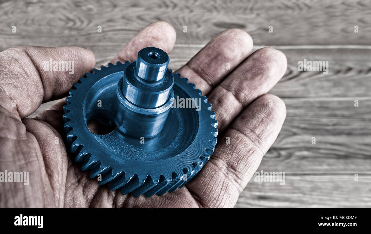 Zahnrad an Palm der Handwerker. Künstlerische Nahaufnahme der Hand mit der dekorativen blauen Zahnrad über einem unscharfen Holz Hintergrund. Stockfoto