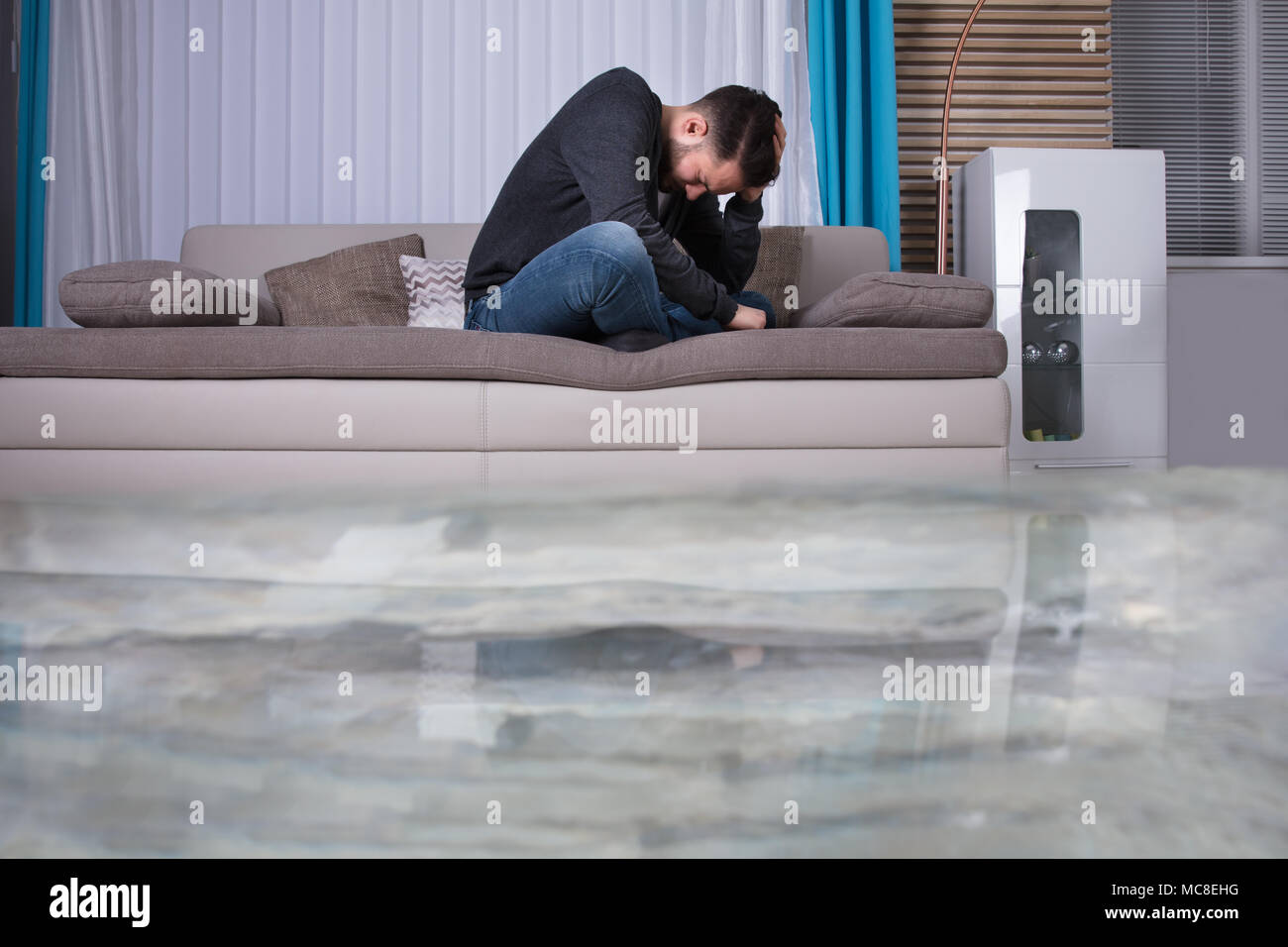 Mann auf Sofa mit Hände auf den Kopf Umkippen in Zimmer überflutet mit Wasser Stockfoto