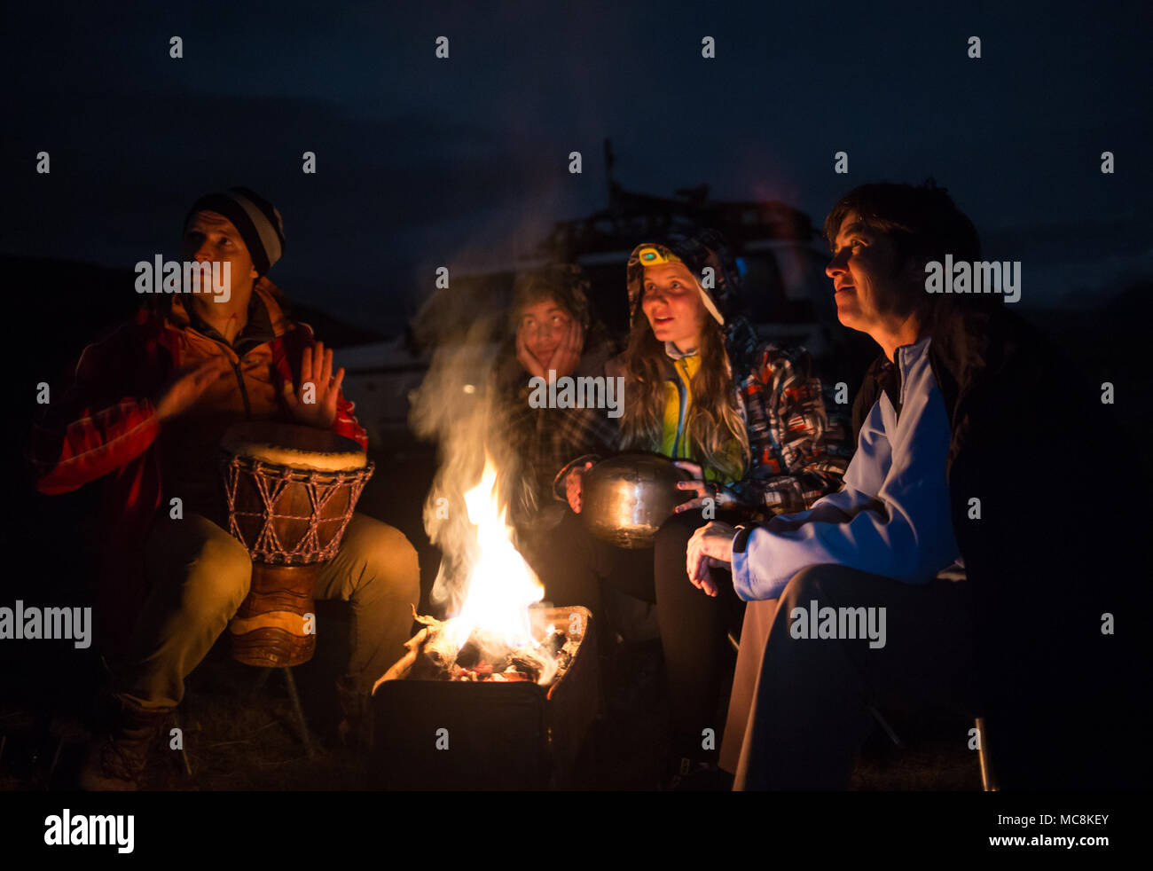 Vier Freunde sitzen in der Nähe der Feuer, Spielen am Schlagzeug und genießen ihre lagerleben an der Natur. Stockfoto