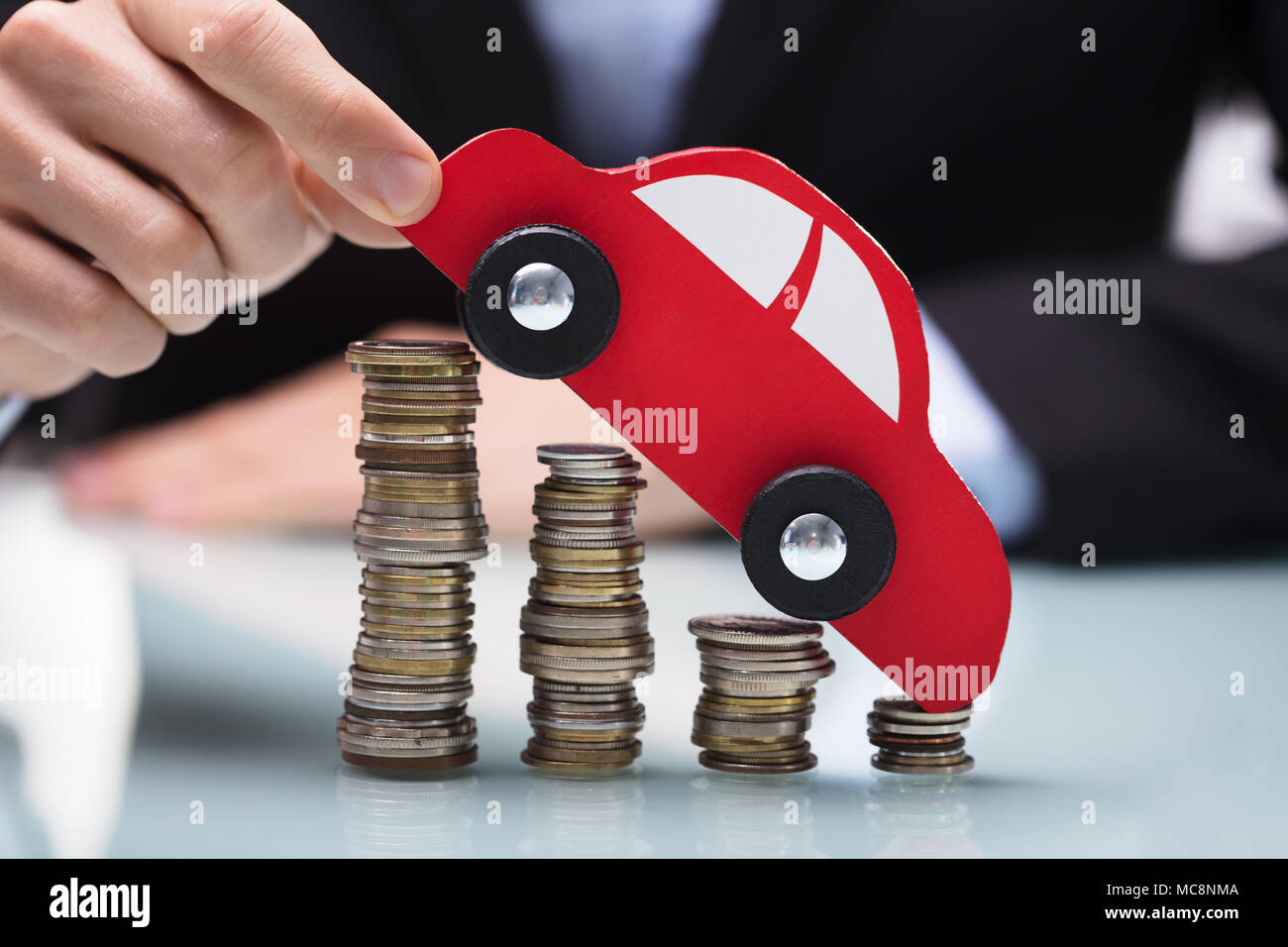In der Nähe von einem Geschäftsmann Hand rotes Auto über Gestapelte Münzen über Schreibtisch Stockfoto