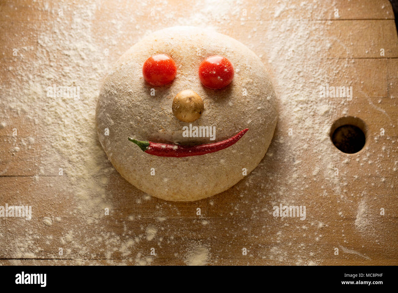 Ball der Teig wie ein glückliches Gesicht, auf einer hölzernen Oberfläche geformt, mit Tomaten und Paprika. Stockfoto