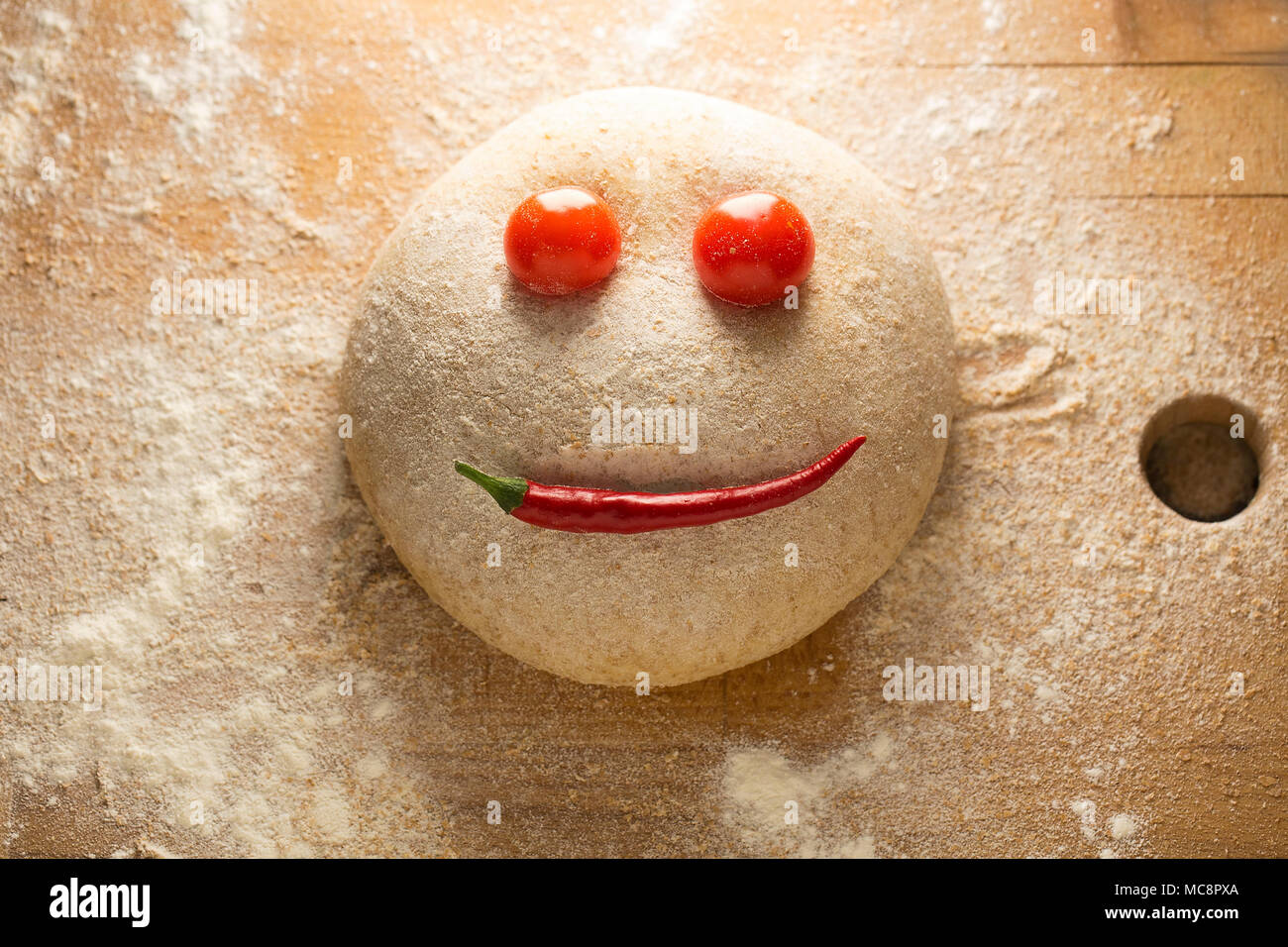 Ball der Teig wie ein glückliches Gesicht, auf einer hölzernen Oberfläche geformt, mit Tomaten und Paprika. Stockfoto