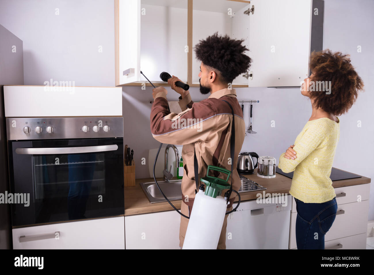 Frau an der Schädlingsbekämpfung Arbeitnehmer Sprühen von Insektiziden auf Haltbarkeit der heimischen Küche Stockfoto