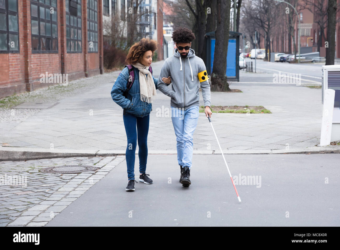 Junge Frau hilft blinden Mann mit weißem Stick beim Überqueren der Straße Stockfoto