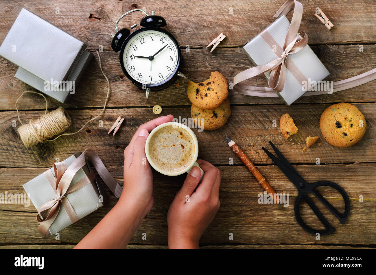 Schöne Frau Hände halten Geschenkbox auf Holz- Hintergrund. Schwarz Wecker, Stift, Schere. Vorbereitung für Geburtstag, Weihnachten, neues Jahr. Lebensstil Stockfoto