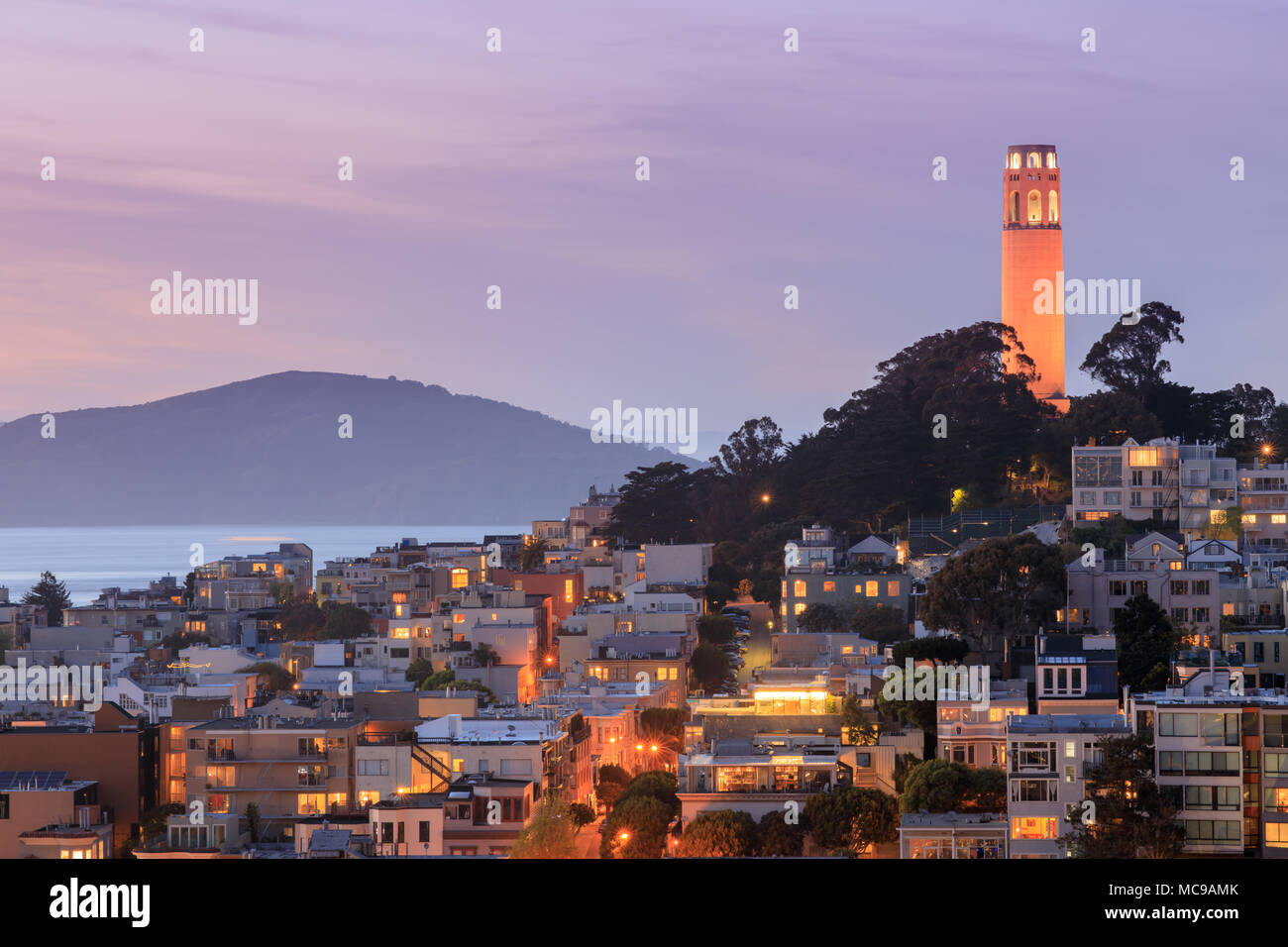 Coit Tower auf Telegraph Hill mit der San Francisco Bay und Angel Island im Hintergrund in der Abenddämmerung. Stockfoto