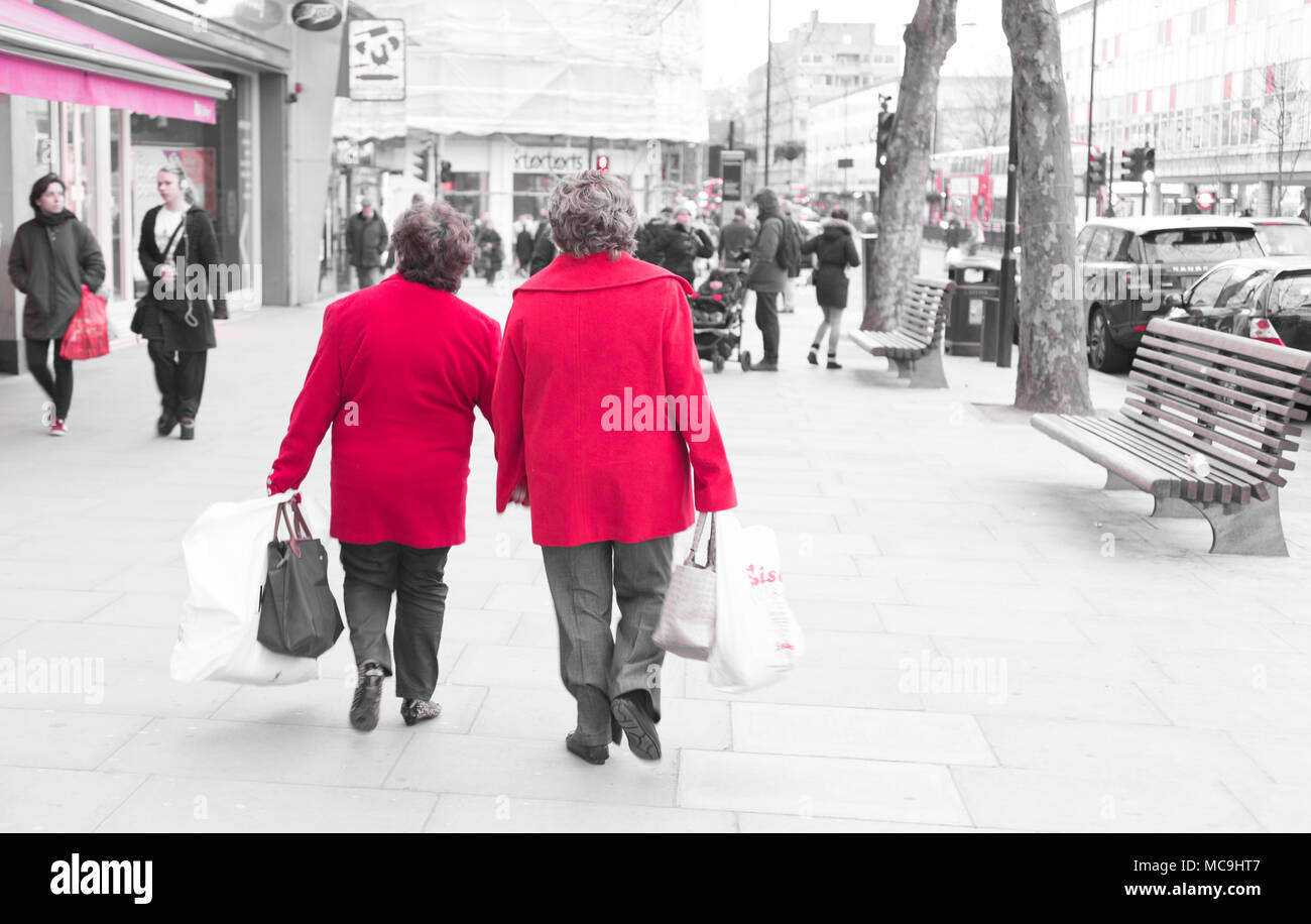 Zwei unkenntlich alte Damen Frauen tragen ein helles Rot winter Jacke zu Fuß auf einer belebten Hauptstraße mit Einkaufstaschen Stockfoto