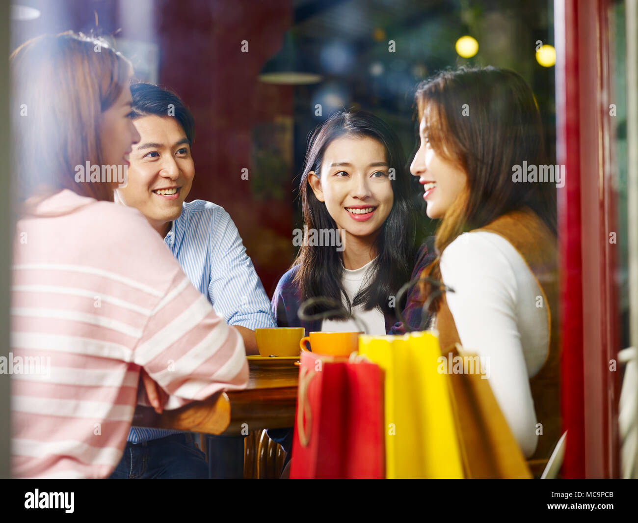 Vier Glückliche junge asiatische erwachsene männliche und weibliche entspannten Plaudern im Gespräch in Coffee Shop nach dem Einkaufen, Schuß durch Fensterglas. Stockfoto