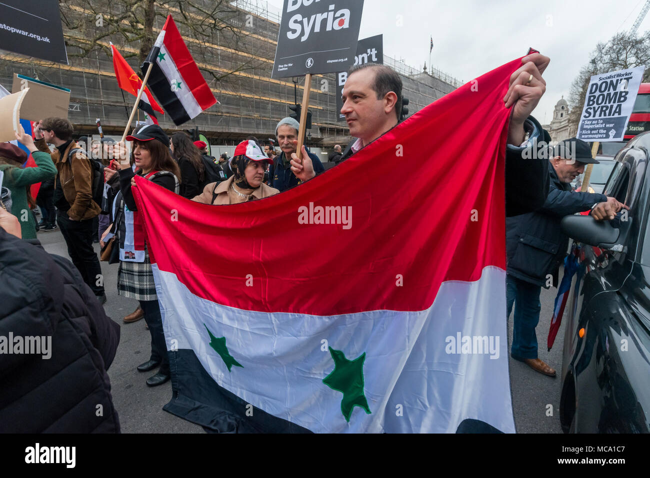 April 13, 2018 - London, UK. 13. April 2018. Personen blockieren, Whitehall in Protest, ein syrischer Flagge. Der Krieg und die Syrer Protest in Downing St stoppen Aufruf für Theresea kann ihre Pläne Syrien mit den USA und Frankreich zur Bombe zu stoppen Nach den Berichten über eine chemische Waffe Angriff gibt. Den Krieg Stoppen in einem Brief von MPs, Gewerkschafter und andere unterzeichnet übergeben und hielt eine Kundgebung auf der gegenüberliegenden Seite von Whitehall, mit Reden von Stop den Krieg und andere Aktivisten. Laut Chanten fortgesetzt und viele der Anwesenden überquerte die Straße draußen Downing Street zu protestieren vor dem Blockieren beide Richtungsfahrbahnen Stockfoto