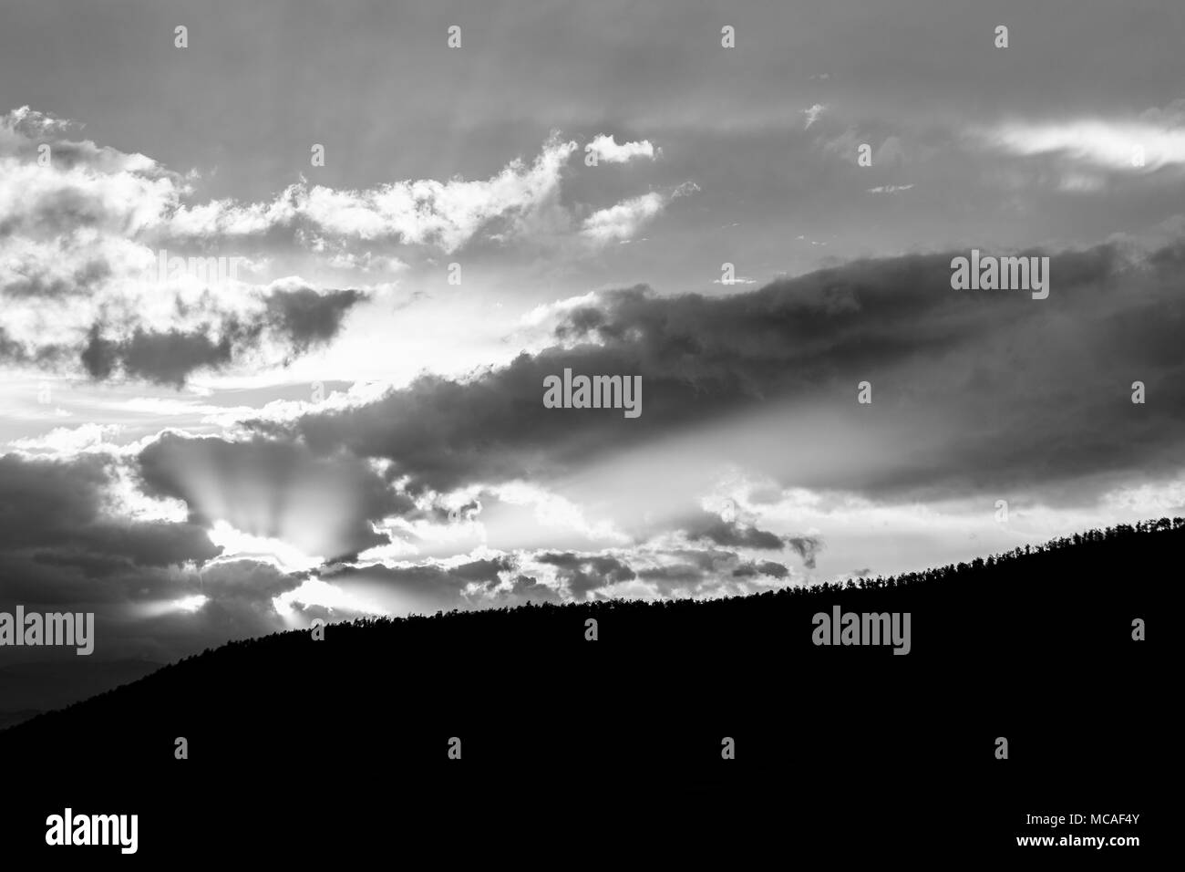 Sonnenuntergang über einem Bäume Linie auf einem Hügel, mit Sonnenstrahlen, die sich durch einige Wolken Stockfoto