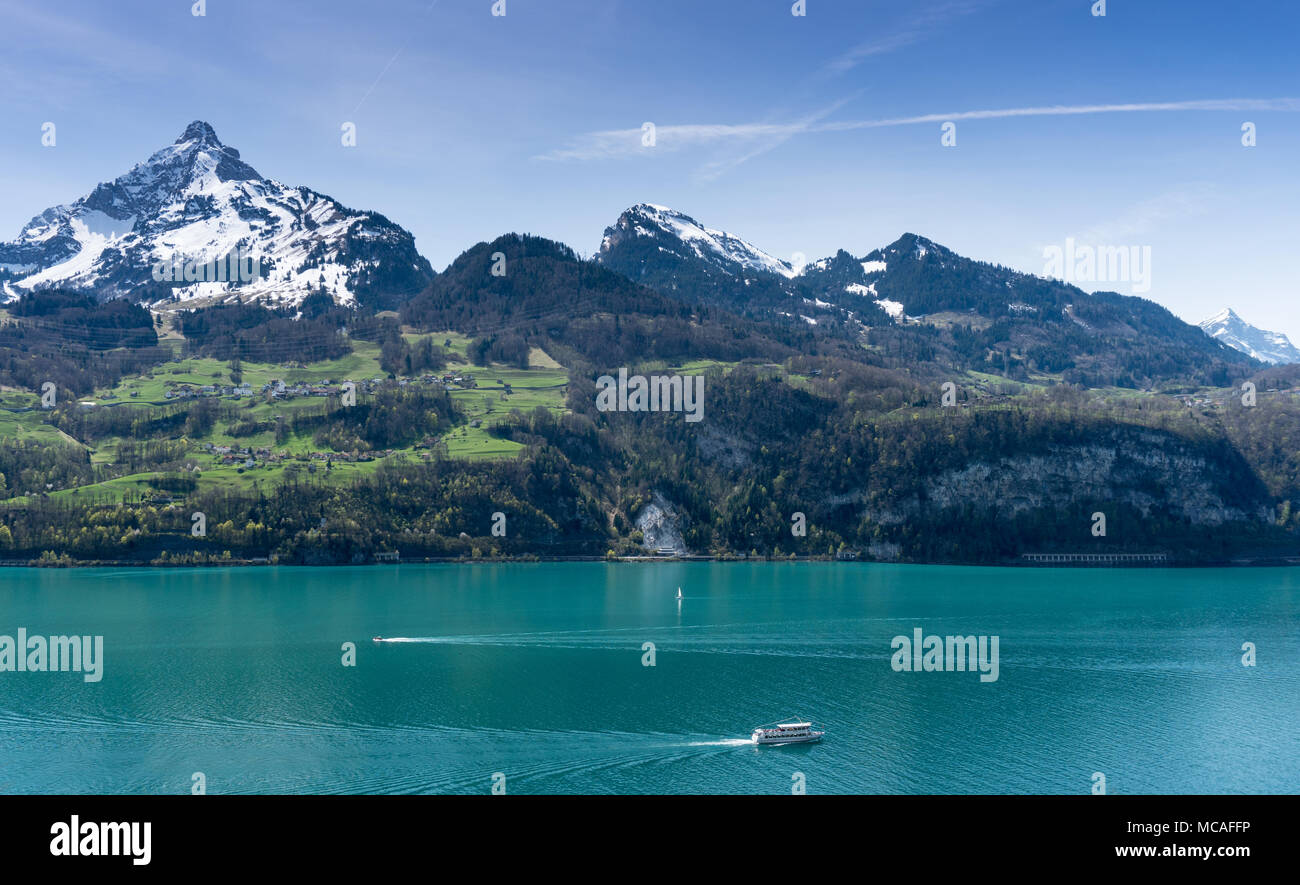 Schöne türkisblaue See Panorama mit schneebedeckten Gipfeln und grünen Wiesen und Wälder und die Boote auf dem See Stockfoto