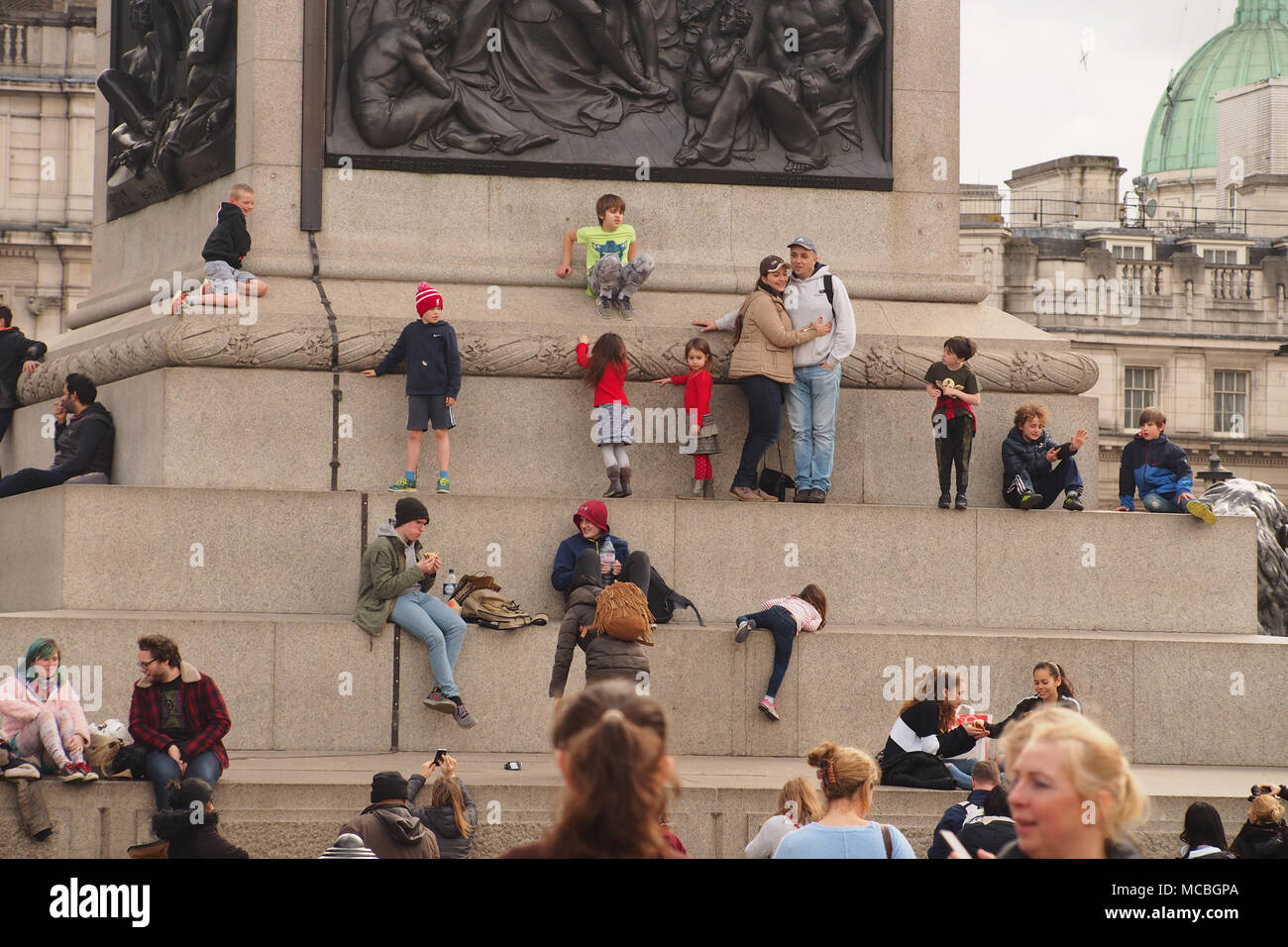 Männer, Frauen und Kinder, sitzen, stehen, klettern und spielen an der Basis der Nelson's Column auf den Trafalgar Square, London Stockfoto