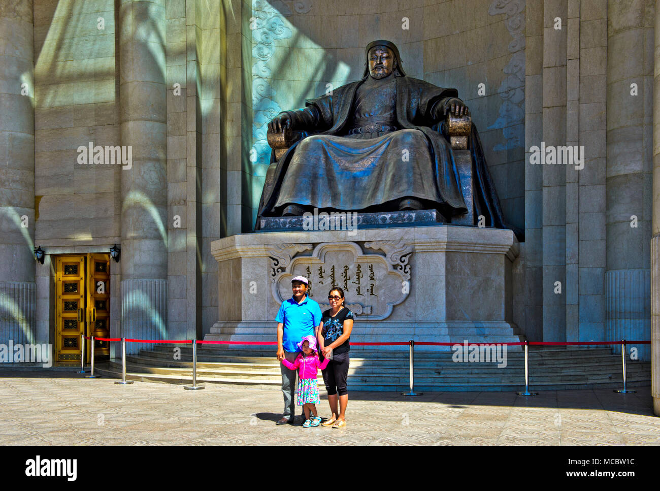 Mongolische Paar mit Kind steht für ein Erinnerungsfoto vor dem Dschingis Khan Denkmal an das Parlamentsgebäude auf Sukhbaatar Platz, Ulaan Stockfoto