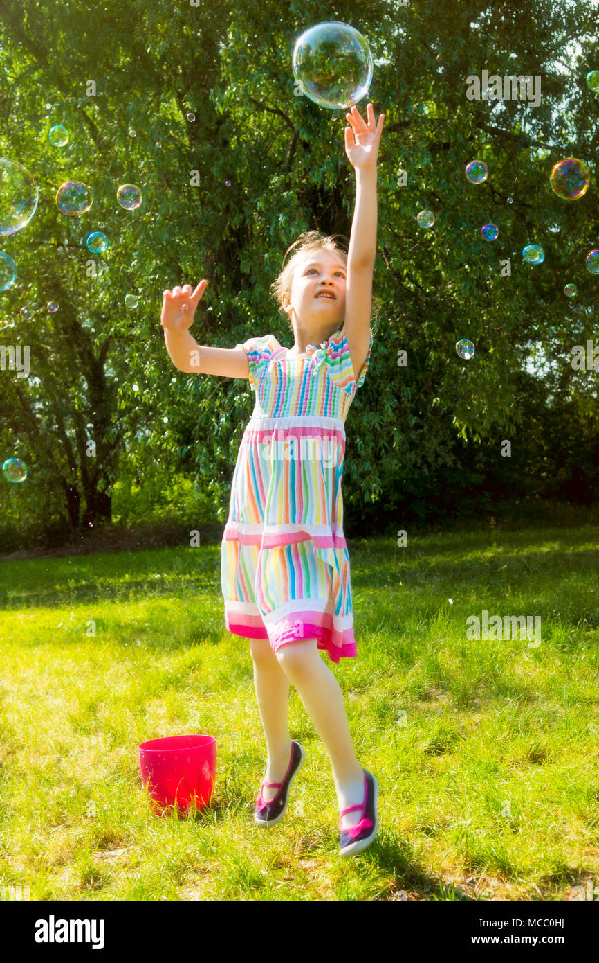 Kleines Mädchen fangen Regenbogen Seifenblasen im Sommer Park. Stockfoto