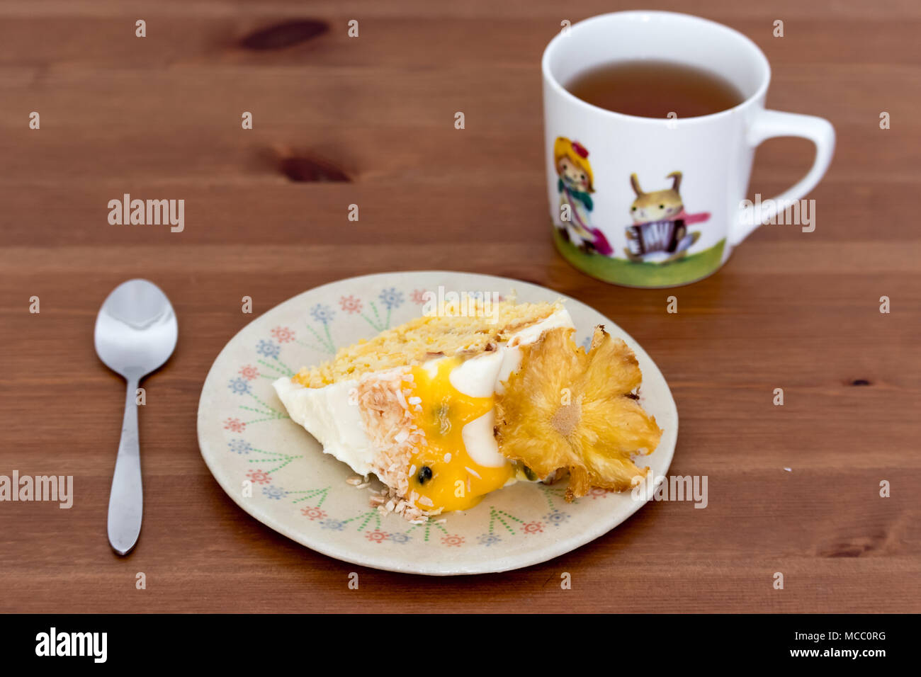 Eine Scheibe Ananas und Kokos Kuchen mit Passionsfrucht Quark, auf handgefertigten Teller serviert mit schwarzem Tee. Stockfoto