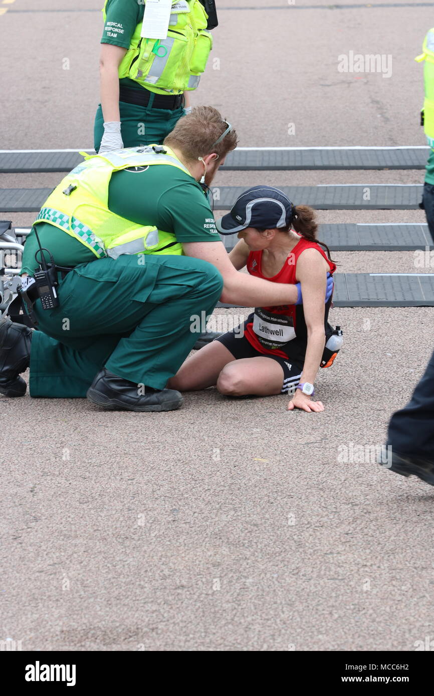 Ein Sanitäter hilft eine Läuferin, die an der Ziellinie nach einem Marathon zusammengebrochen Stockfoto