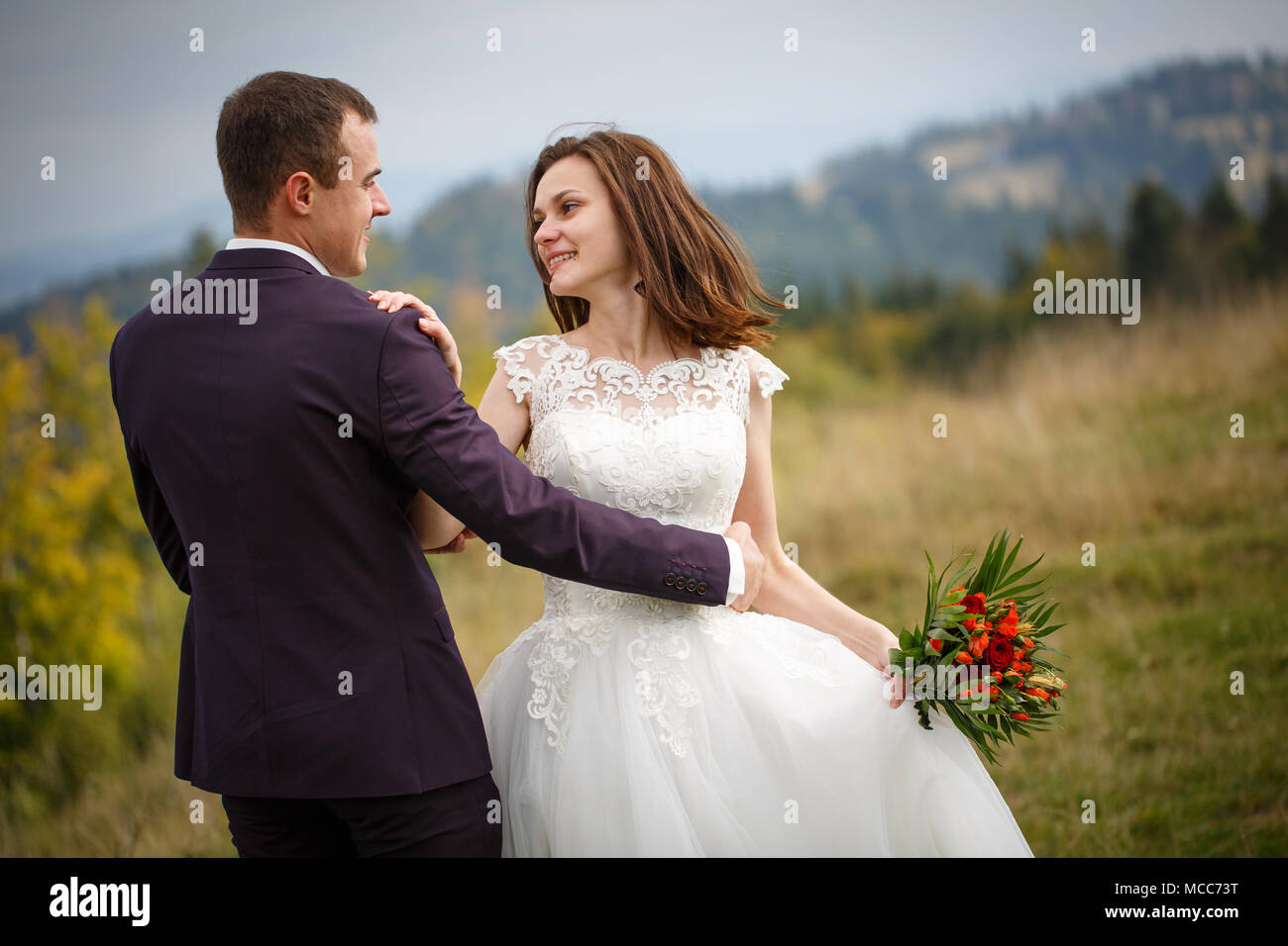 Paar ein frisch verheiratetes Paar sind in den Bergen. Stilvolle Braut mit einem Blumenstrauß küsst den Bräutigam. Liebe, Treue und das Spiegeln Konzept. Berg Stockfoto