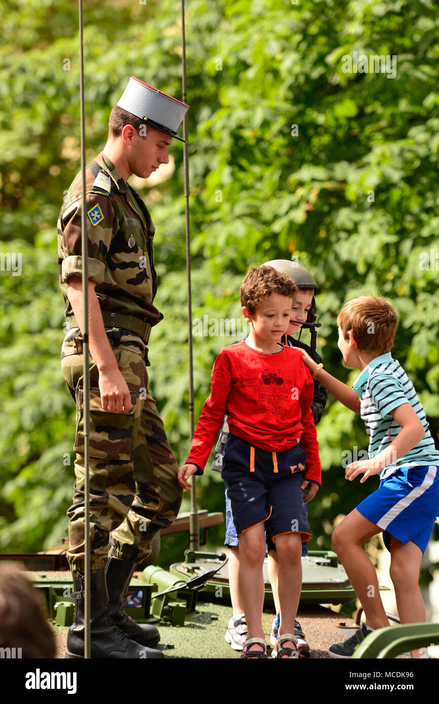 Ein französischer Soldat geduldig beobachtet, wie Kinder auf einem militärischen Tank während einer Militärparade zum Tag der Bastille in Paris spielen. Stockfoto