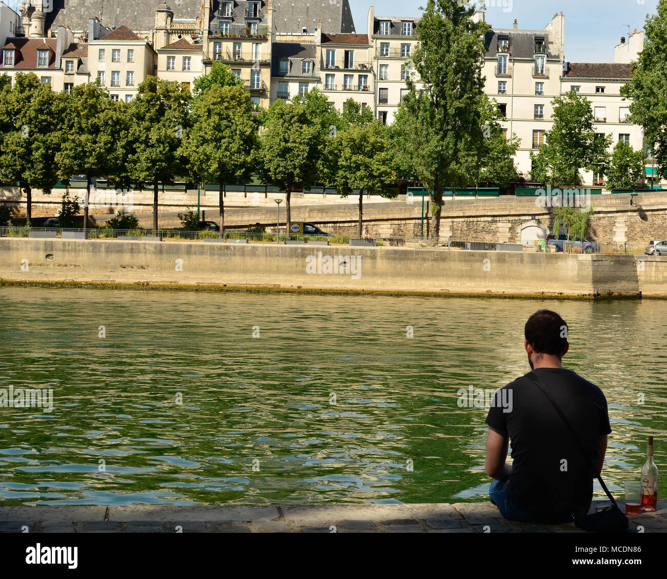 Ein Mann sitzt alleine mit einer Flasche Wein, entspannen Sie am Ufer der Seine in Paris. Stockfoto