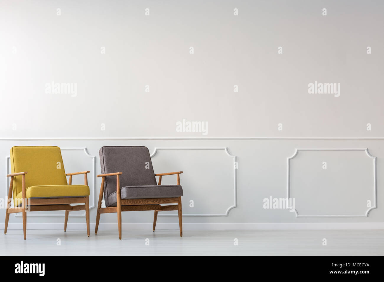Grau und Gelb Holz Sessel gegen weiße Leiste an der Wand im Wohnzimmer Innenraum Stockfoto