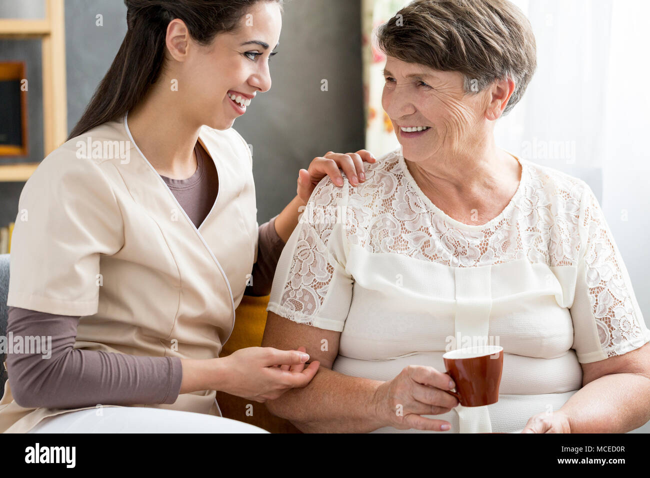 Schöne freiwillige fröhlich im Gespräch mit einem älteren Patienten, trinken Tee Stockfoto