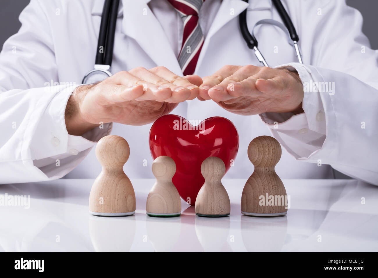 Doctor's Schützende Hand Holz- Familie und rotes Herz auf weißem Schreibtisch Stockfoto