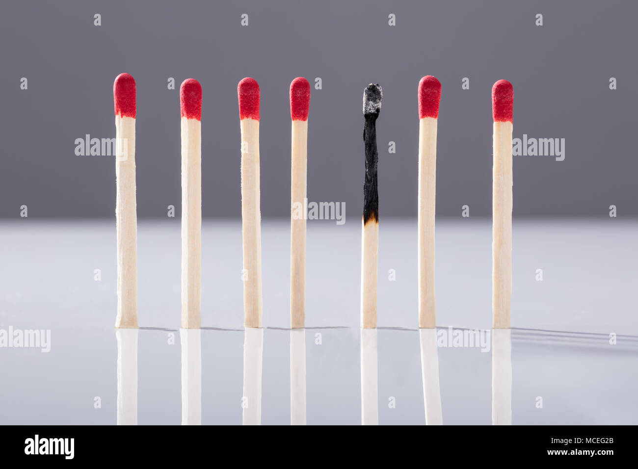 Verbrannt Streichholz getrennt durch rote Matchsticks gegen grauer Hintergrund Stockfoto