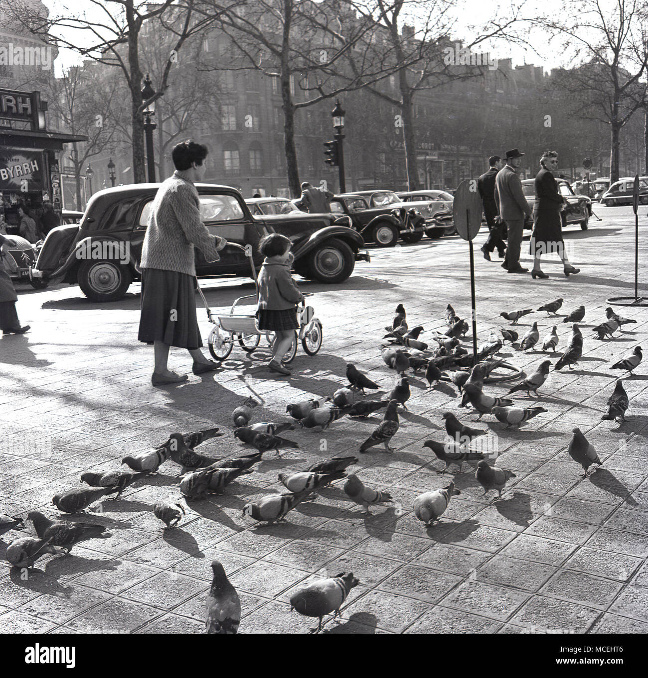 1950er Jahre, historische, Paris, Frankreich, eine Mutter mit einem kleinen Kind an der Tauben auf eine breite Bürgersteig mit parkenden Autos der Ära. Stockfoto