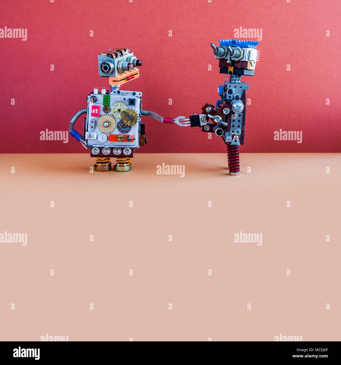 Zwei Roboter begrüßen sich. Handshake von Kybernetischen mechanischen Cyborgs. Kreatives Design Roboter Spielzeug, rote Wand Braun, Hintergrund. Platz kopieren Stockfoto