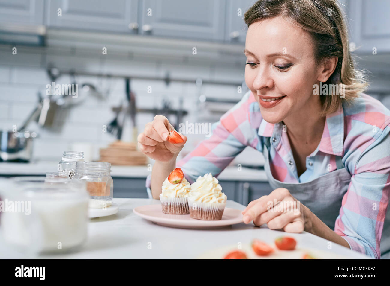 Attraktive Kaukasisch weiblich Konditor dekorieren leckere Cupcakes mit frischen Erdbeeren und glücklich lächelnd Stockfoto