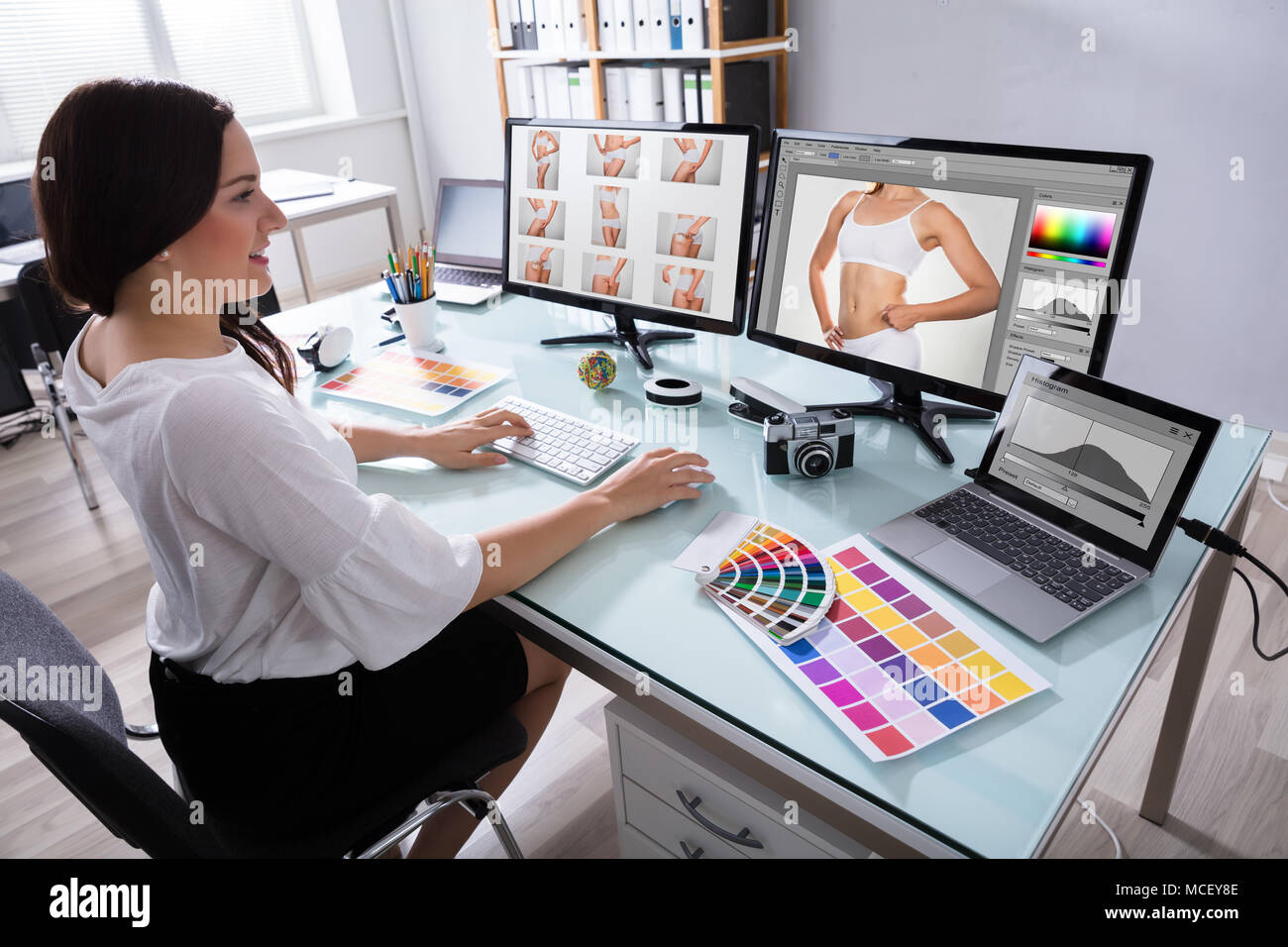 Glückliche junge weibliche Designer Arbeiten mit Fotos auf mehreren Computer am Arbeitsplatz Stockfoto