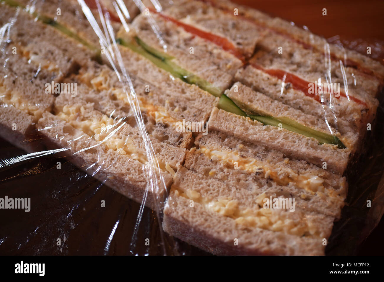 Eine Auswahl an Sandwiches in Streifen mit Kruste und auf einer Platte mit sauberem Film abdecken, um sie frisch zu halten. Stockfoto