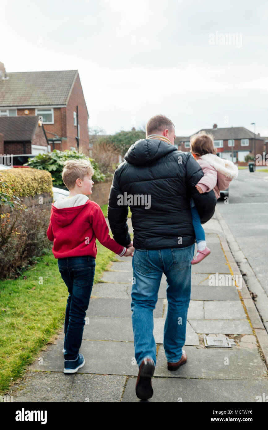 Rückansicht eines reifer Mann auf der Straße mit seinen Kindern. Hält er seine Söhne und seine Tochter. Stockfoto