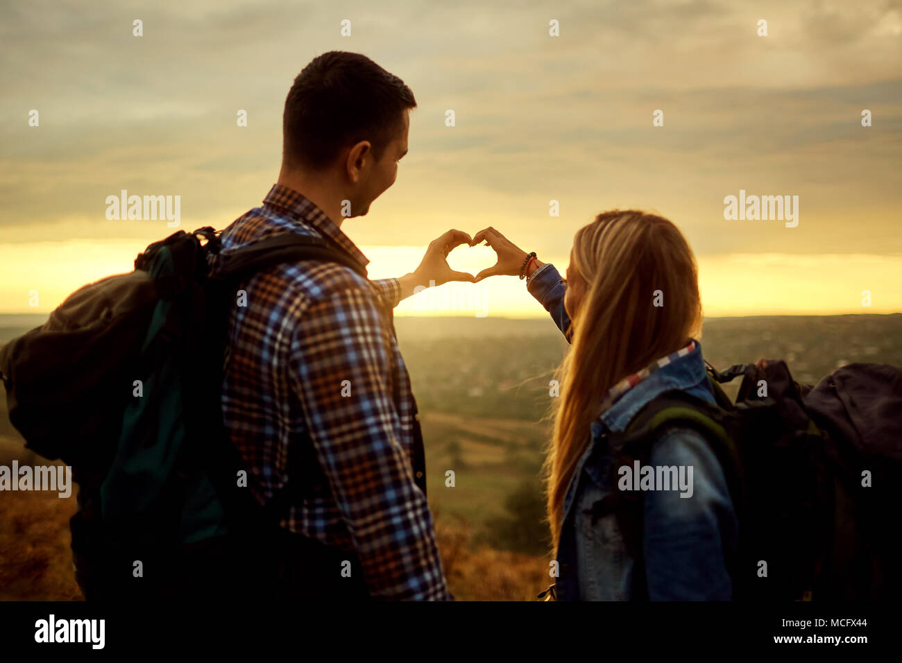 Ein paar Touristen mit Rucksäcken, ein Symbol für die Herzen, mit den Händen auf die Natur am Abend bei Sonnenuntergang. Ansicht von hinten. Stockfoto