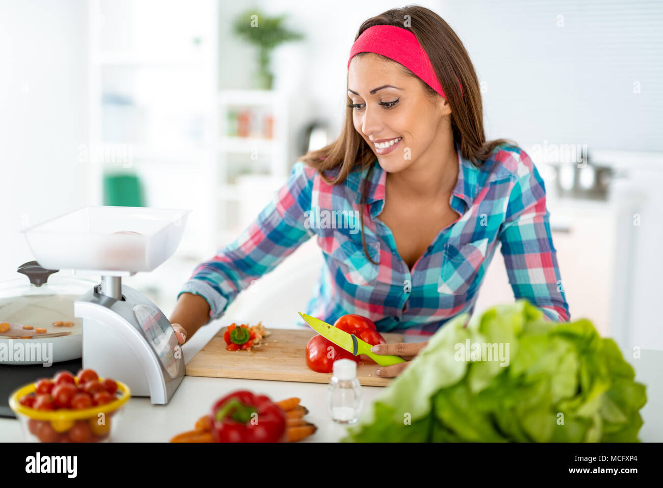 Schöne junge Frau, die gesunde Mahlzeit in der heimischen Küche. Sie ist mit einem Gewicht von etwas über Küchenwaagen. Stockfoto