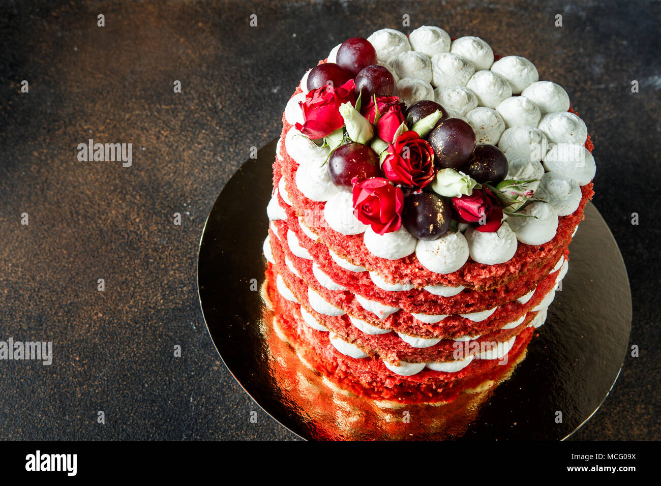 Horizontal oben Blick auf viele rote Schwamm und weißen Bizet Schichten von bunten Kuchen mit bizet, Trauben und Rosen Stockfoto