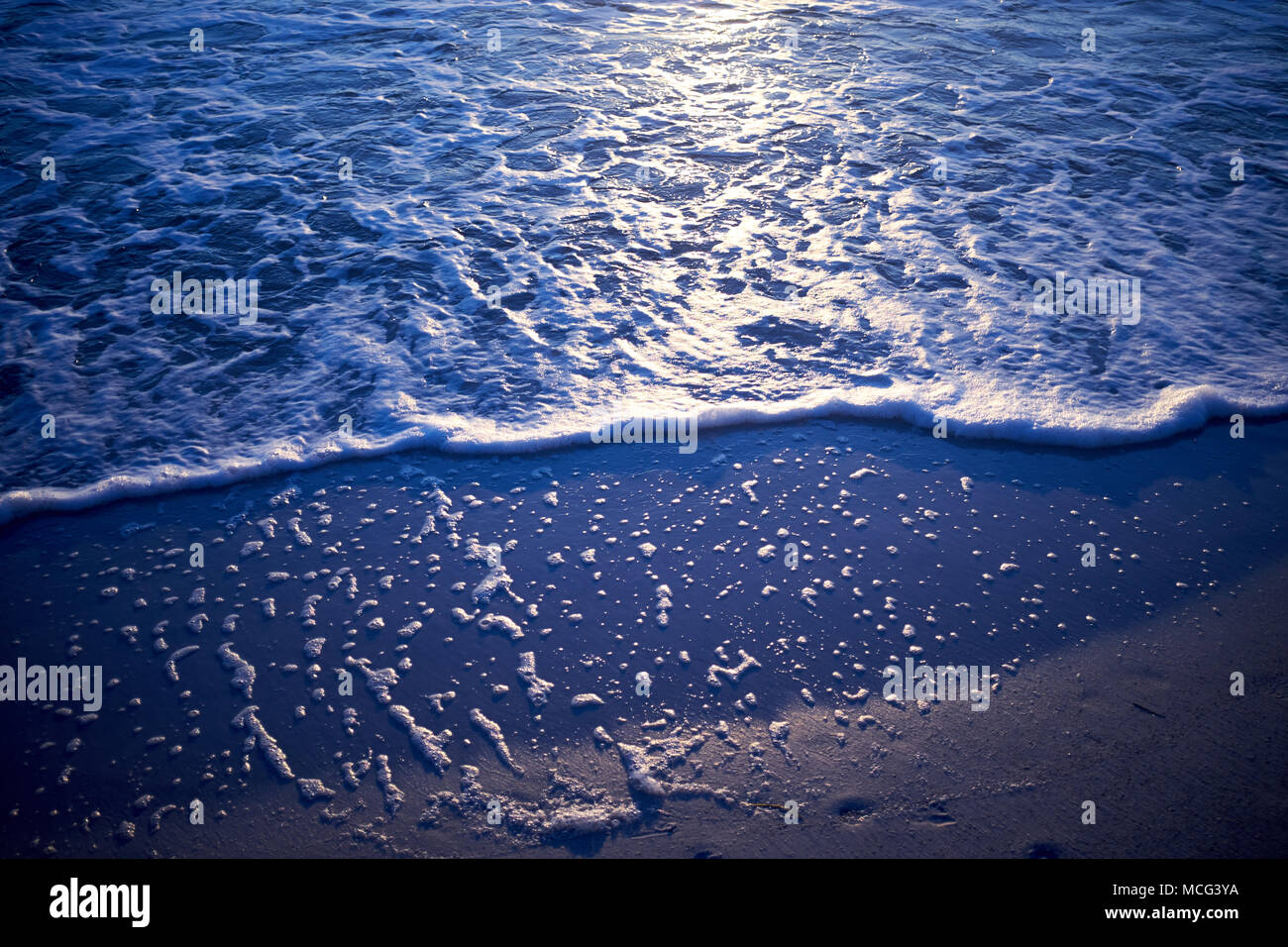 Wellen am Sandstrand mit Reflektion der Sonneneinstrahlung. Stockfoto