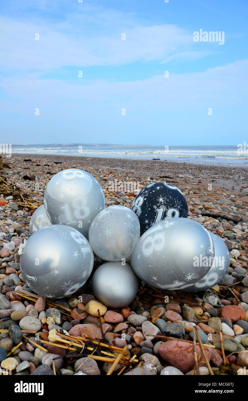 Ein Bündel von 18. Geburtstag party Helium Gas Ballons, die als Einstreu am Strand gelandet sind. Stockfoto