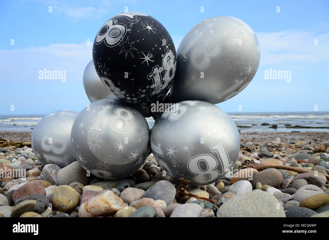 Ein Bündel von 18. Geburtstag party Helium Gas Ballons, die als Einstreu am Strand gelandet sind. Stockfoto