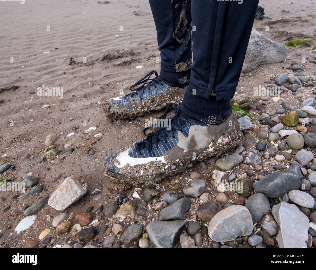 Schlamm bedeckt Junior Football Trainer auf einem nassen Sand- und Felsstrand in Morecambe Bay, England, Großbritannien am 11. April 2018. Stockfoto