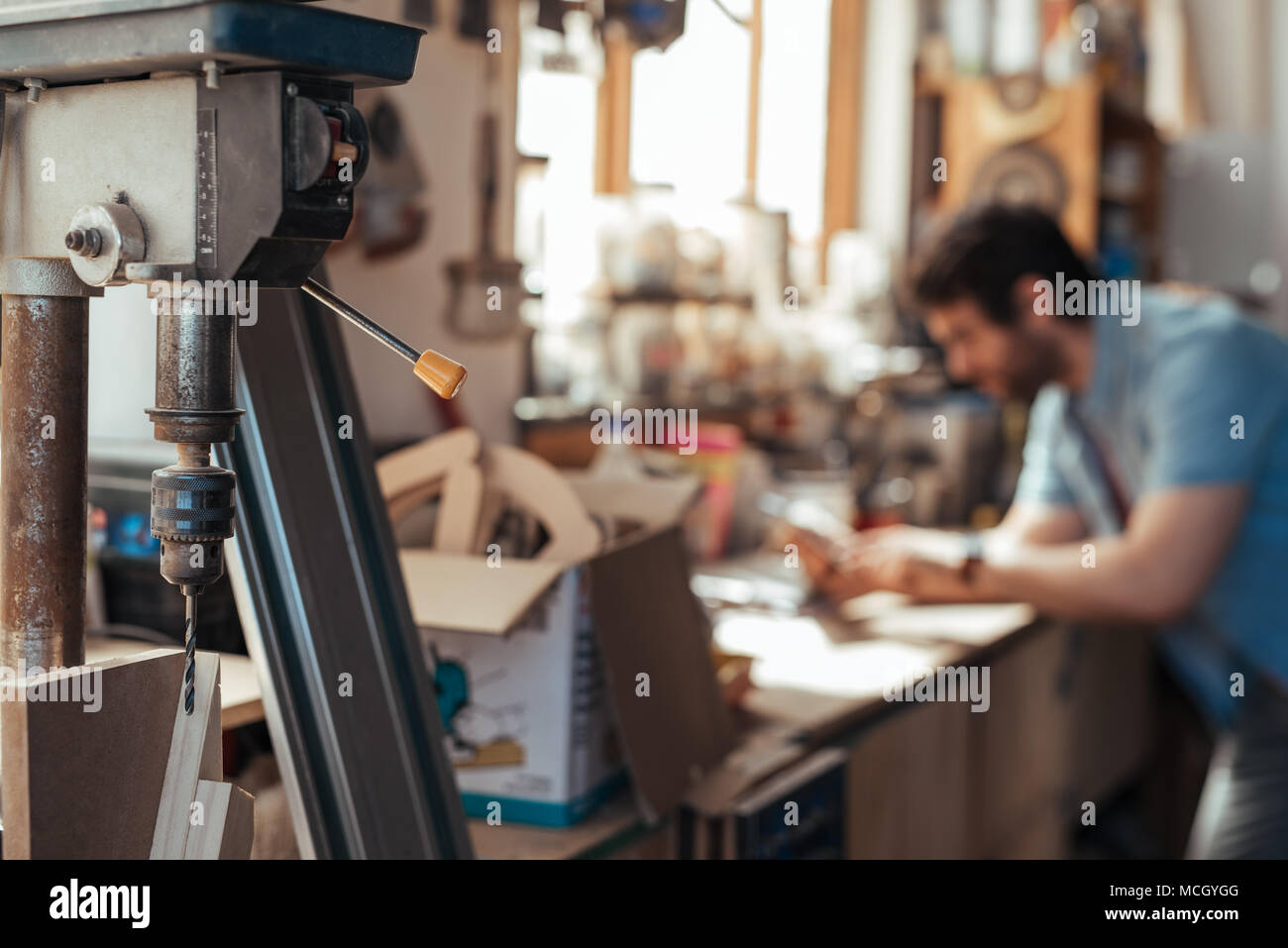 Nahaufnahme von einer Bohrmaschine in einem Holzbearbeitung Workshop mit einem Zimmermann mit einem digitalen Tablet an Werkbank im Hintergrund Stockfoto