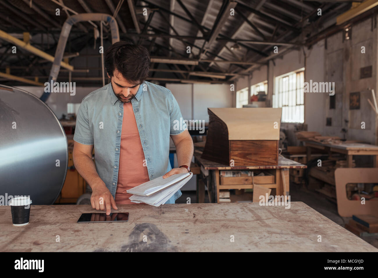 Qualifizierte junge woodworker stehend an einer Werkbank in seiner Schreinerei mit einem digitalen Tablet-PC und einem Notebook Designs Stockfoto