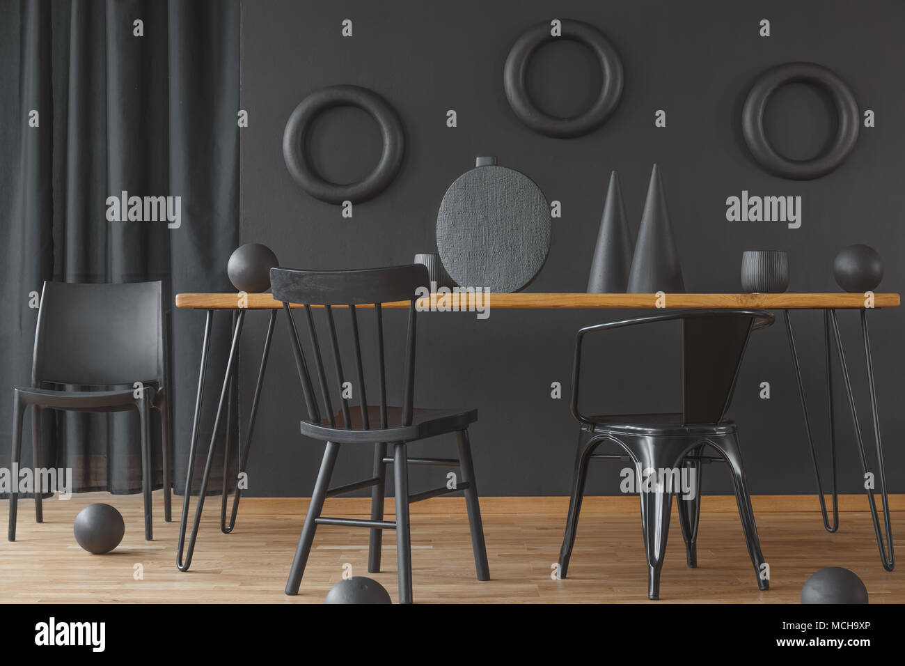 Schwarz, einfarbig Esszimmer Innenraum mit Holz- Tabelle steht gegen eine Wand mit Ringen Dekoration Stockfoto