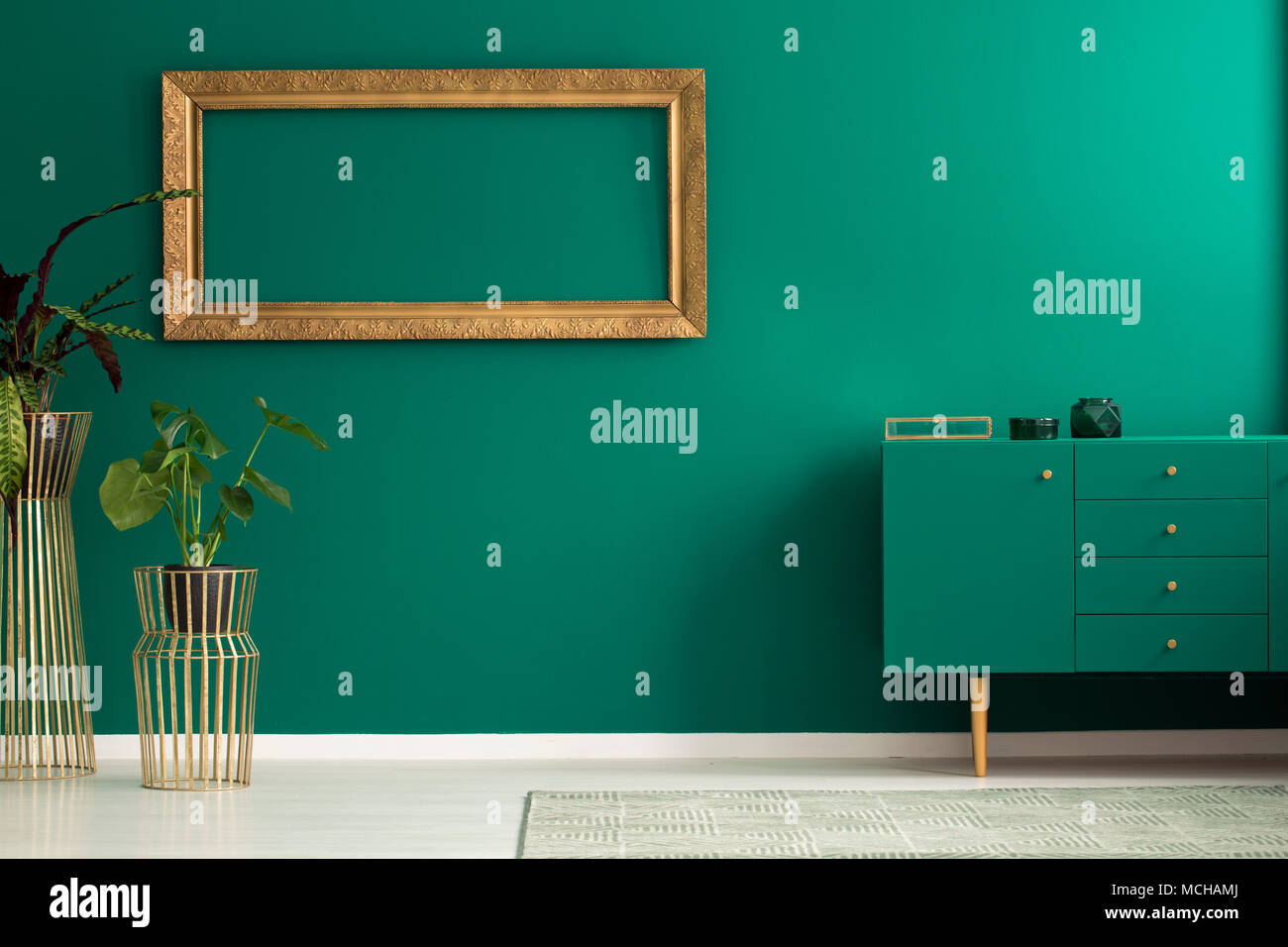 Anlage gegen die Wand mit leeren Gold frame in einfachen Wohnzimmer Einrichtung mit grünen Schrank Stockfoto