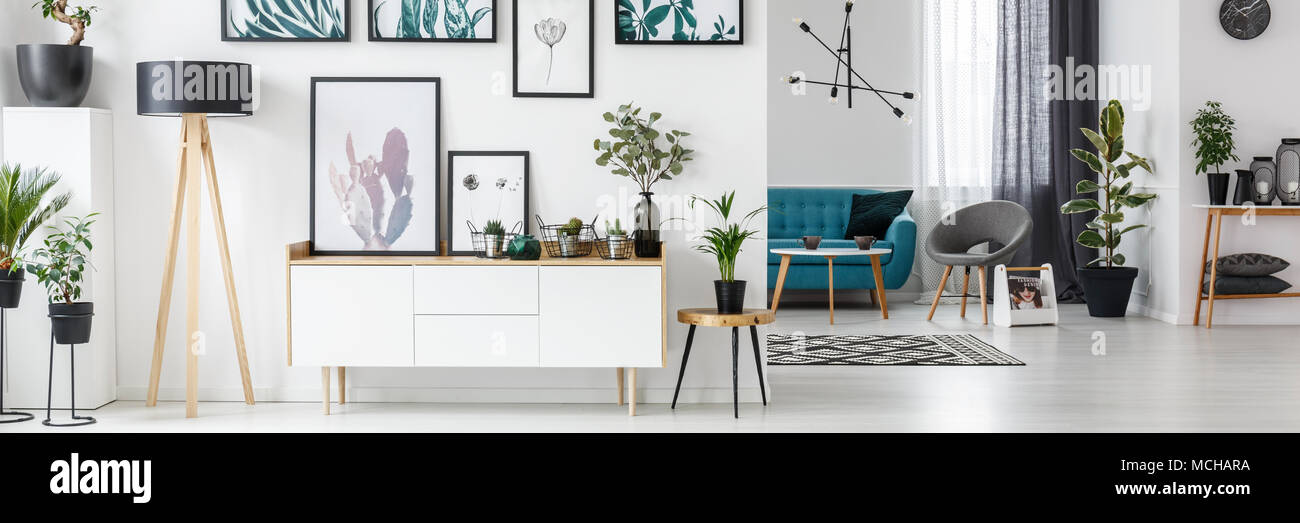 Weiß Wohnzimmer mit Galerie an der Wand, Holzschrank und frische Pflanzen Stockfoto
