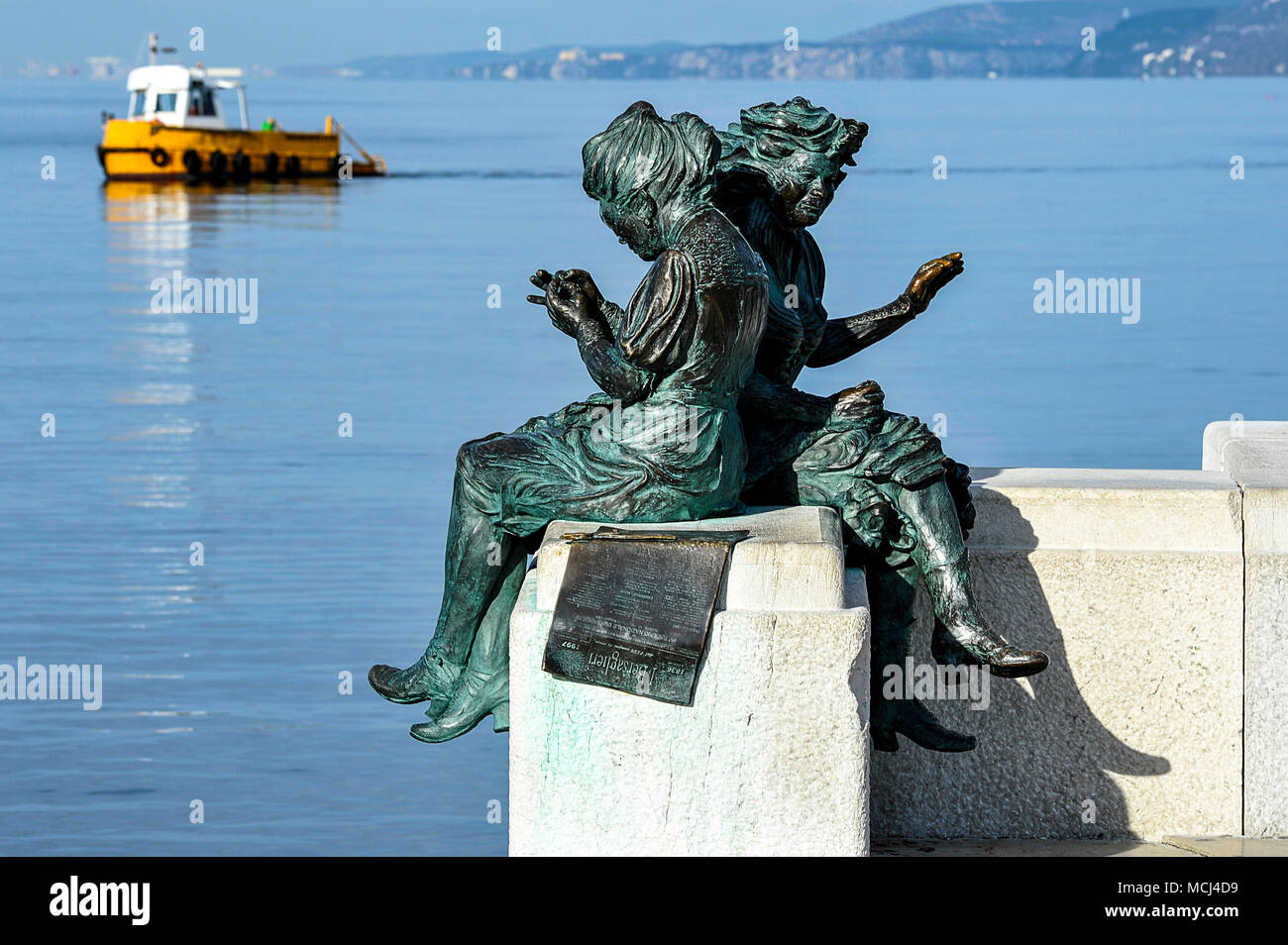 Italia, Friaul Julisch Venetien, Triest. Il Lato mare di Piazza Unità ospita La Scala Reale in cui si trova La statua in Bronzo raffigurante due Donne intente eine cucire La Bandiera italiana, l'Opera porta Il Nome di'Le Ragazze di Trieste". | Italien, Friaul Julisch Venetien, Triest. Eine Bronzestatue von Frauen nähen die italienische Flagge entlang der Uferpromenade Stockfoto