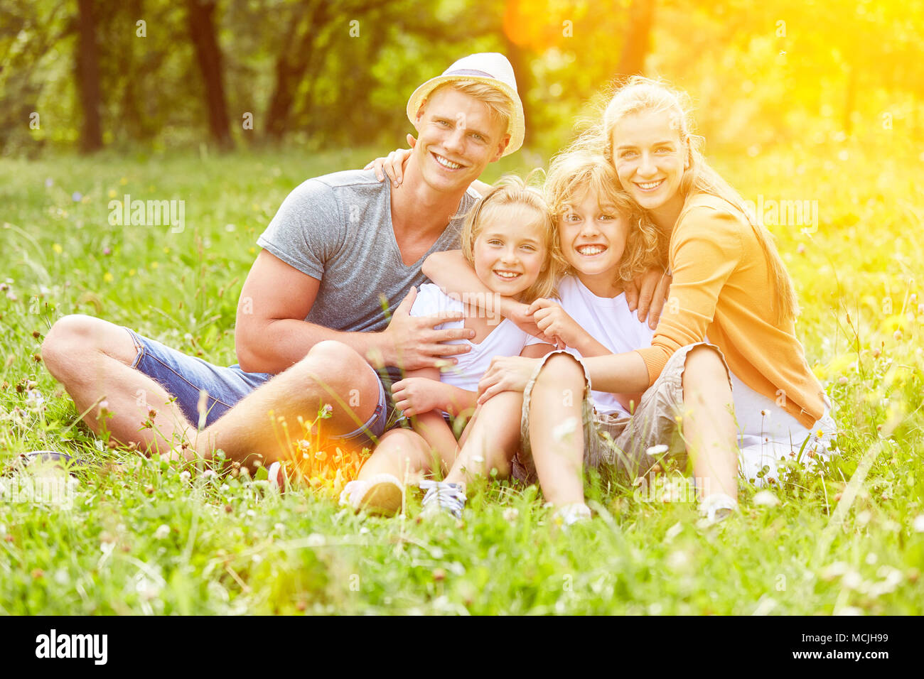 Glückliche Eltern und ihre zwei Kinder sind sitzen zusammen auf einer Wiese im Garten Stockfoto