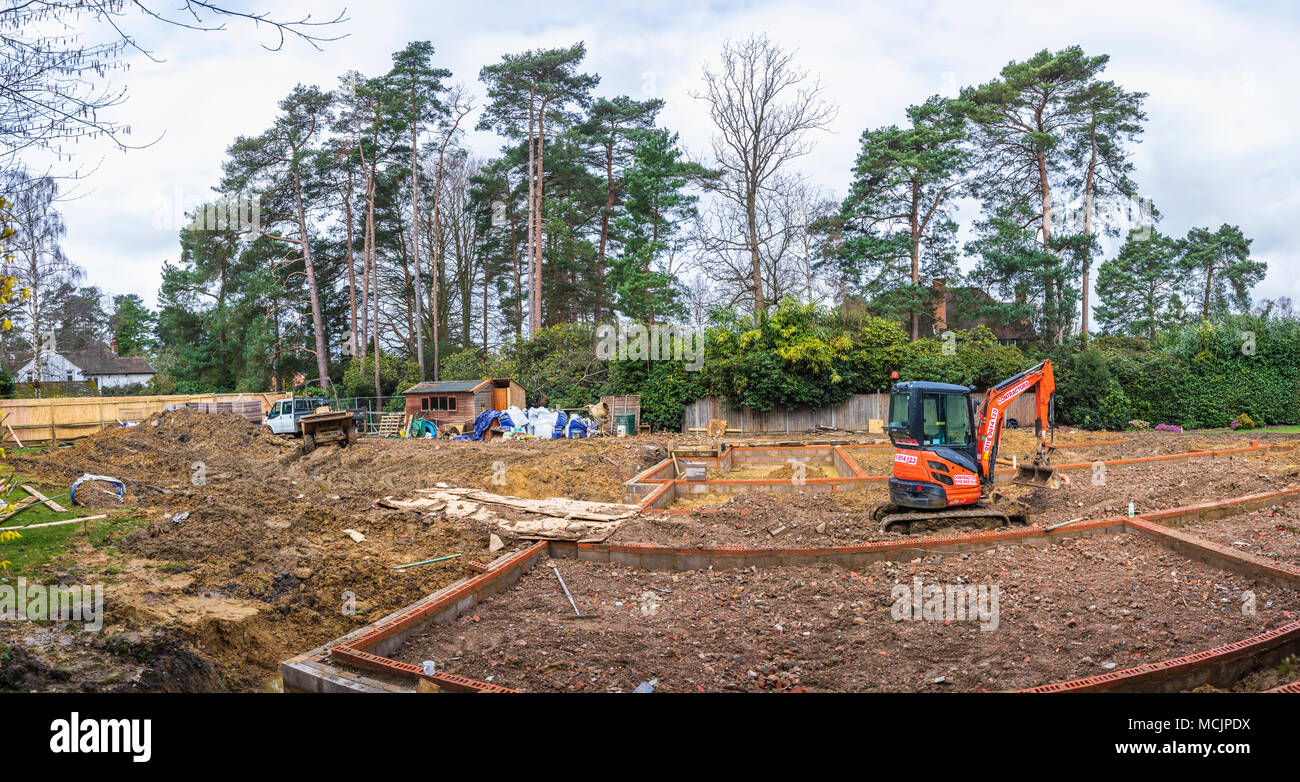 Orange Hitachi schwerem mechanische Digger in den Grundstein für ein neues Haus im Bau auf einer Baustelle in Surrey, Südosten, England, Grossbritannien Stockfoto